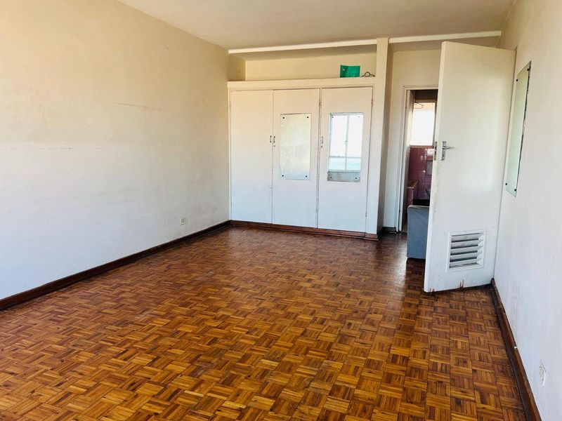 An empty bedroom featuring original parquet flooring and built-in cupboards, requiring cosmetic updates to restore its appeal.