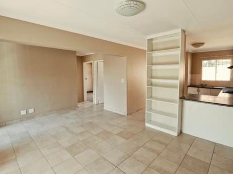 An open-plan living and kitchen area featuring tiled flooring, built-in shelving, and functional kitchen cabinetry with a hob and extractor fan.