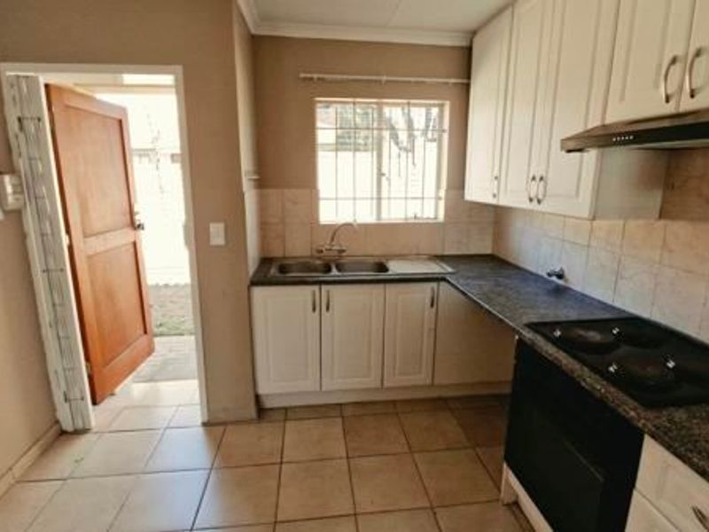 A functional kitchen featuring built-in cabinetry, a double sink, electric hob, oven, and extractor fan, with direct access to the exterior.