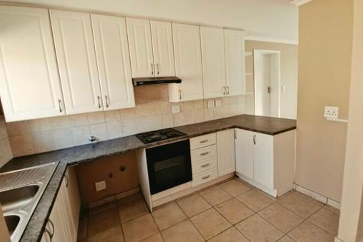 A clean, functional kitchen featuring white cabinetry, dark laminate countertops, built-in oven with gas hob, and tiled flooring.
