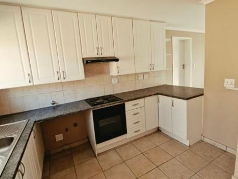 A clean, functional kitchen featuring white cabinetry, dark laminate countertops, built-in oven with gas hob, and tiled flooring.