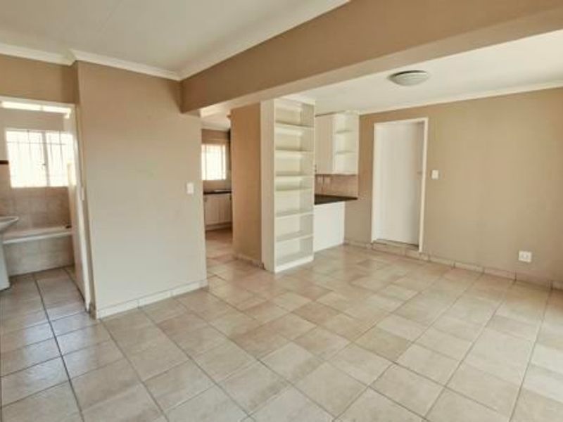 An open-plan living area featuring tiled flooring, built-in shelving, and a view into the adjacent kitchen and bathroom spaces.