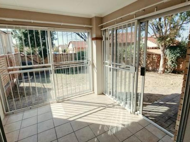 A covered patio area featuring tiled flooring, sliding glass doors with security gates, and direct access to the rear garden.