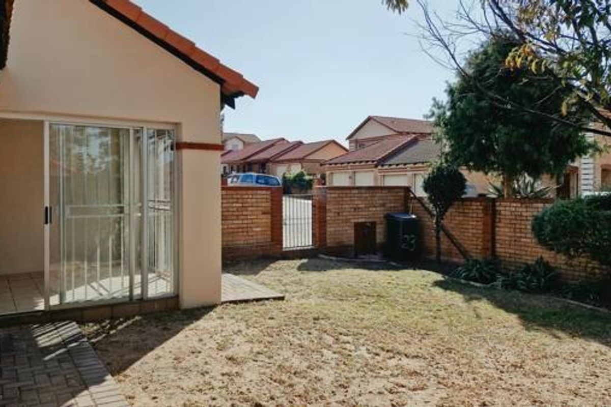 A rear view of the property featuring a small private garden, a paved walkway, and a covered patio area with sliding glass doors.