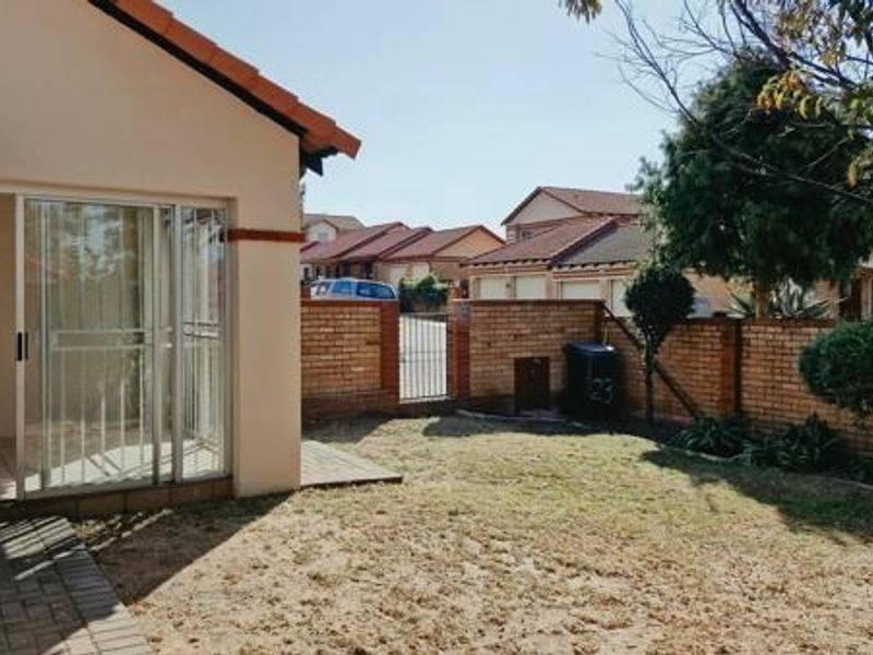 A rear view of the property featuring a small private garden, a paved walkway, and a covered patio area with sliding glass doors.
