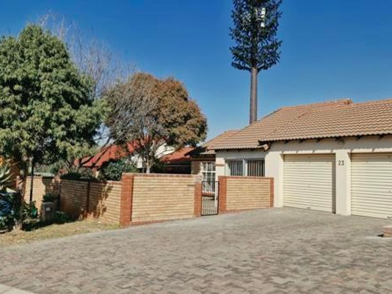 Front view of a residential property featuring a double garage with roll-up doors, a paved driveway, and a brick boundary wall.