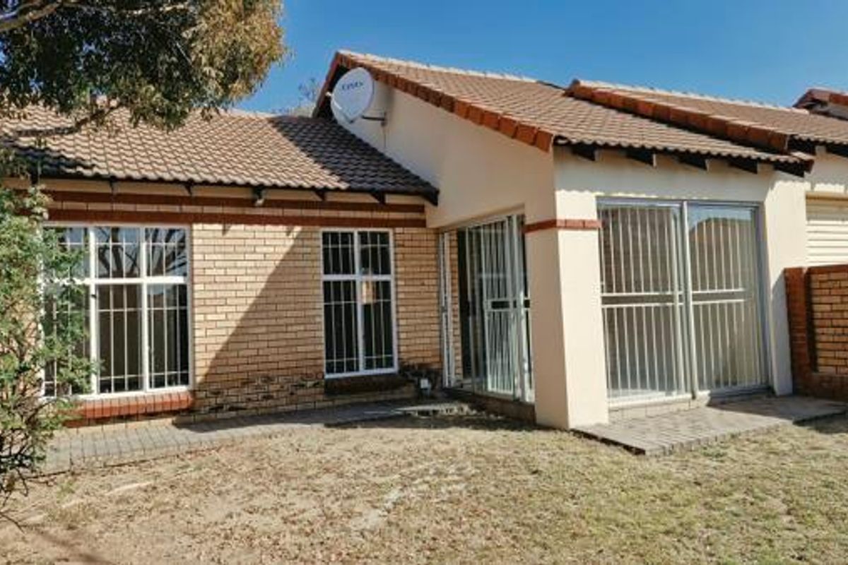 Rear view of a single-story brick house featuring a tiled roof, security-barred windows, and a paved patio area leading to a garden.