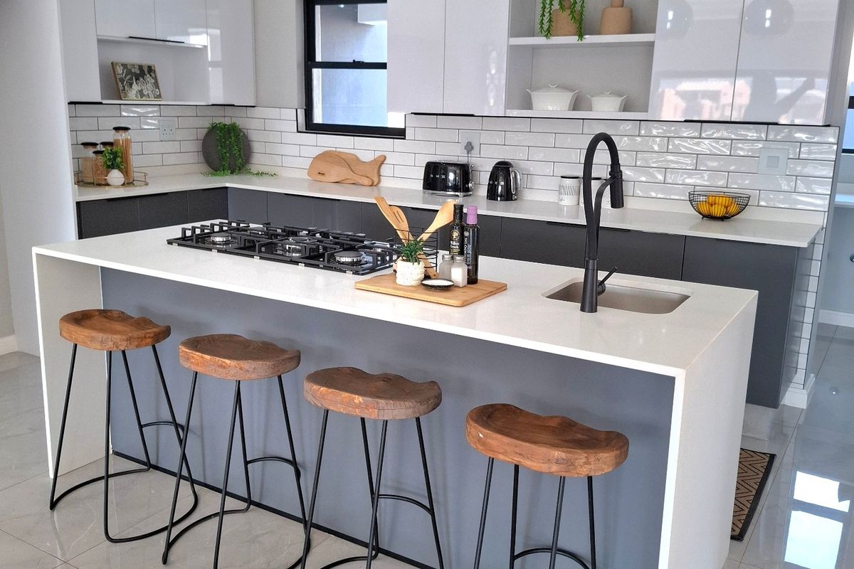 Modern kitchen featuring a central island with a gas cooktop, undermount sink, quartz countertops, and sleek white and grey cabinetry with subway tile backsplash.