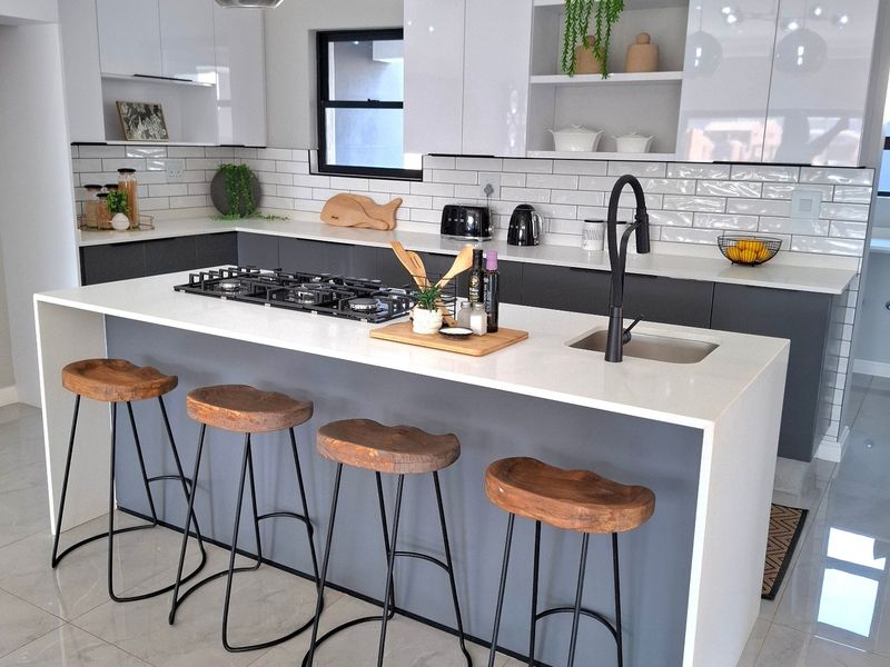Modern kitchen featuring a central island with a gas cooktop, undermount sink, quartz countertops, and sleek white and grey cabinetry with subway tile backsplash.