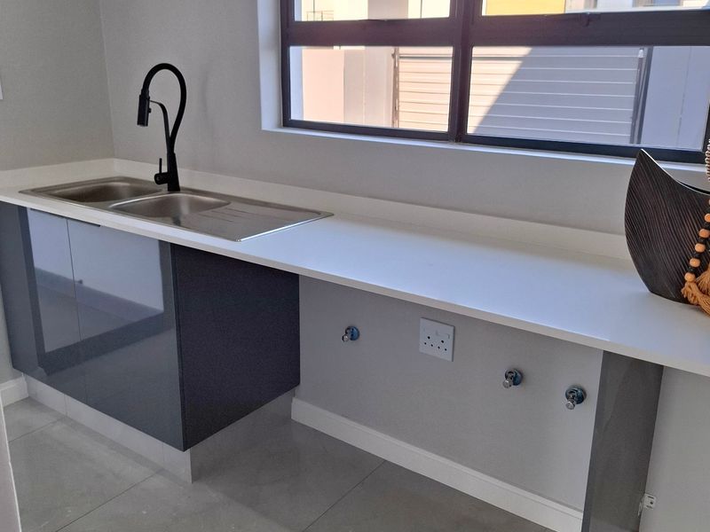 Modern laundry area featuring a sleek stainless steel sink, black faucet, stone countertop, and dedicated plumbing connections for appliances.