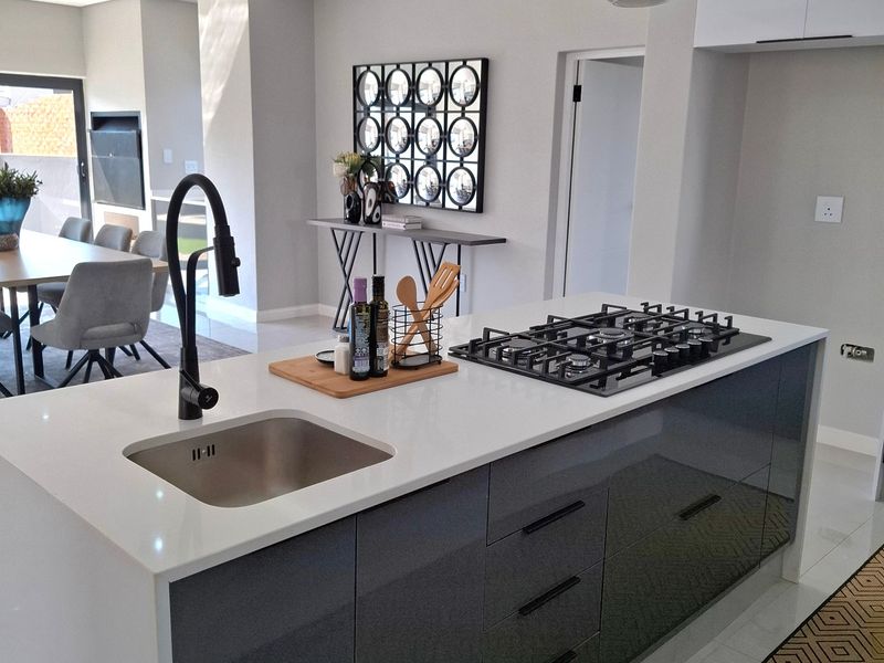 Modern open-plan kitchen featuring a sleek island with a gas hob, undermount sink, and contemporary pendant lighting, seamlessly flowing into the living and dining area.