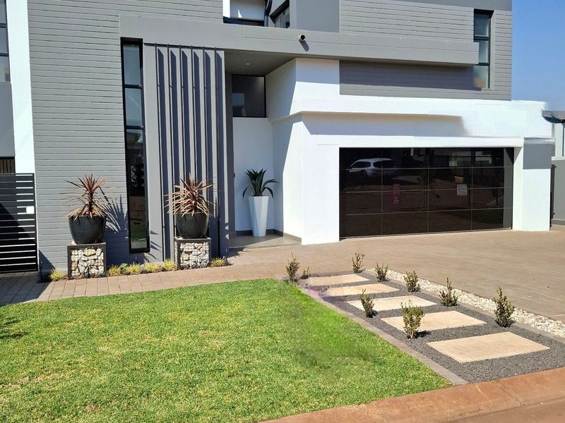 Modern double-story residential home featuring a contemporary facade, paved driveway, integrated double garage, and well-maintained front garden with stepped pathway.