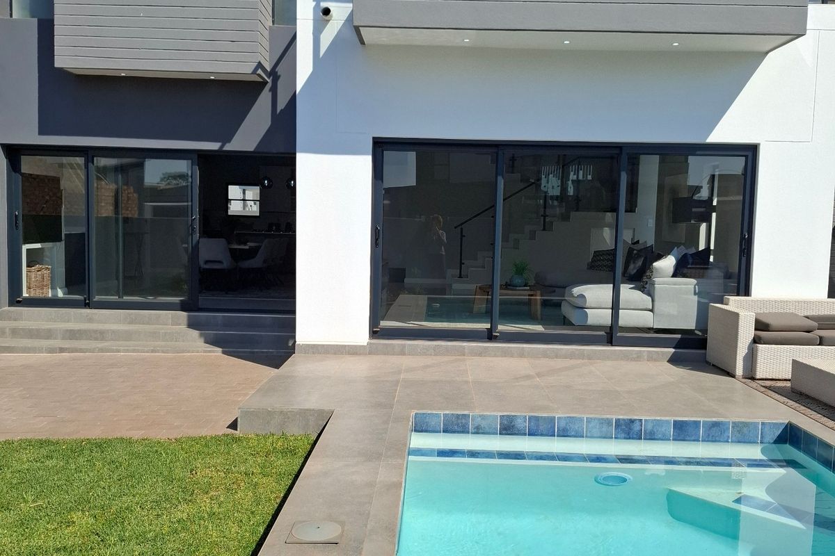 Modern rear exterior view featuring a swimming pool, tiled patio area, large sliding glass doors, and an upper-level balcony with glass balustrades.