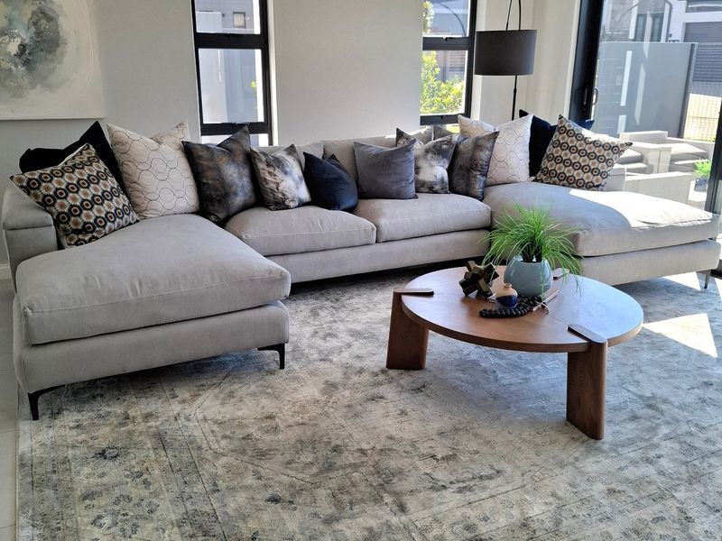 A bright and modern living room featuring recessed ceiling details with cove lighting, large windows, and sliding glass doors leading to the exterior.