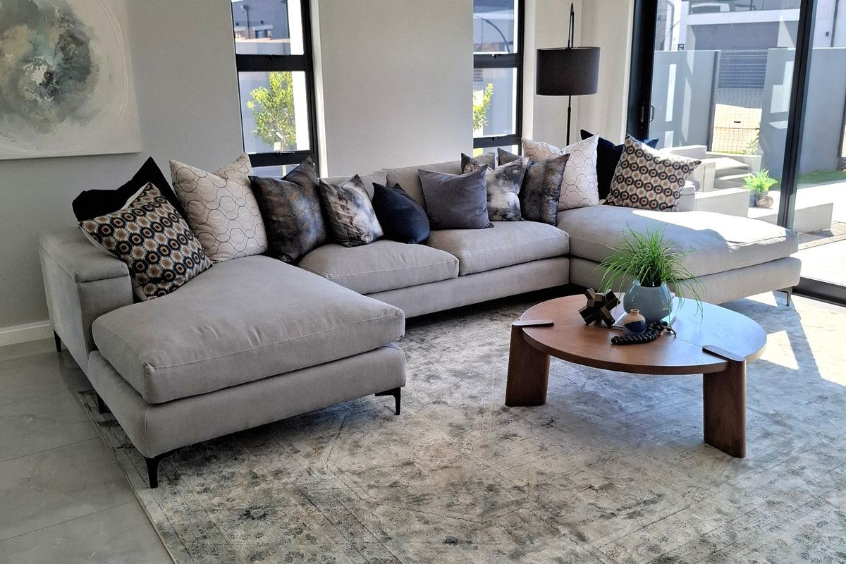 Modern living room featuring a recessed ceiling, large aluminium-framed windows, and sliding glass doors leading to the exterior, finished with neutral tiled flooring.
