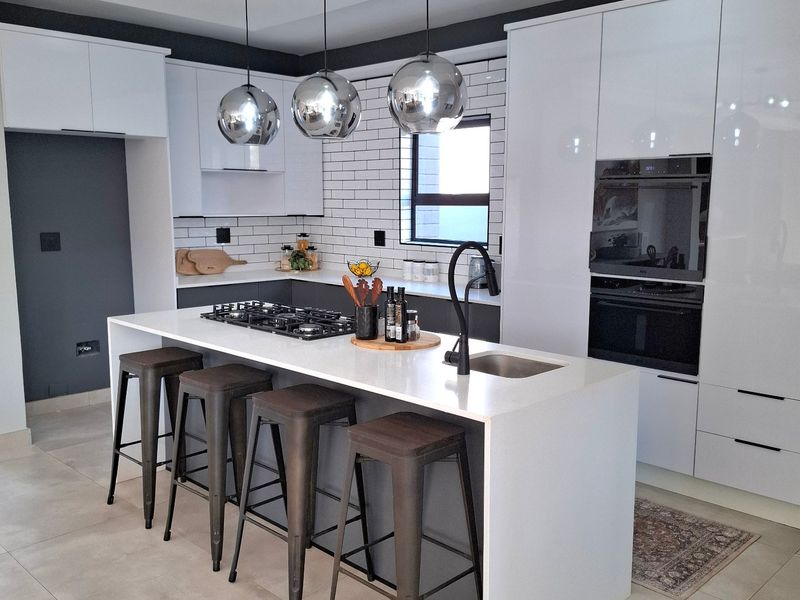 Modern kitchen featuring a central island with gas hob, sleek white cabinetry, subway tile backsplash, and high-end built-in appliances.