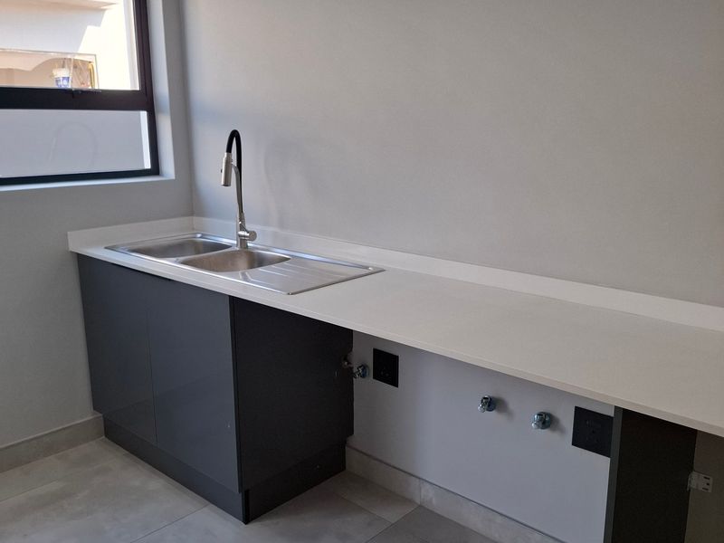 A clean, modern laundry area featuring a stainless steel sink, gooseneck faucet, stone countertop, and dedicated plumbing connections for appliances.