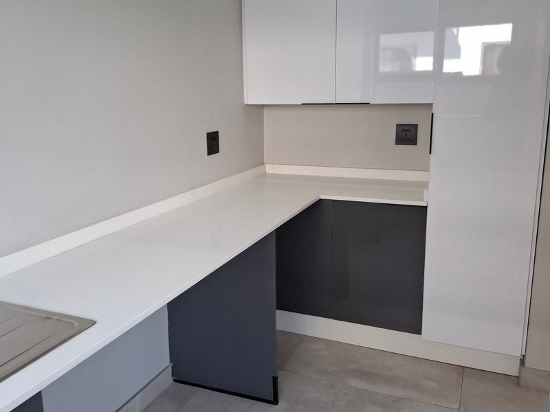 A modern, clean scullery area featuring sleek two-tone cabinetry, stone countertops, and large format floor tiles, providing a functional and contemporary prep space.