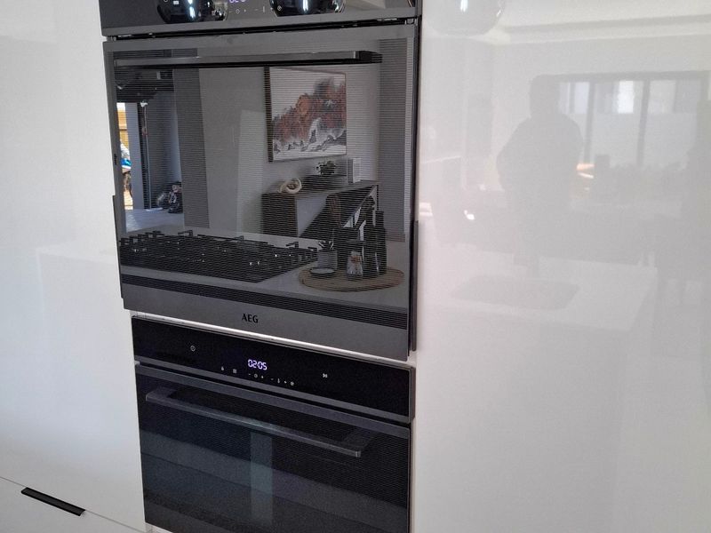 Modern kitchen featuring high-gloss white cabinetry and integrated AEG built-in oven and microwave appliances.