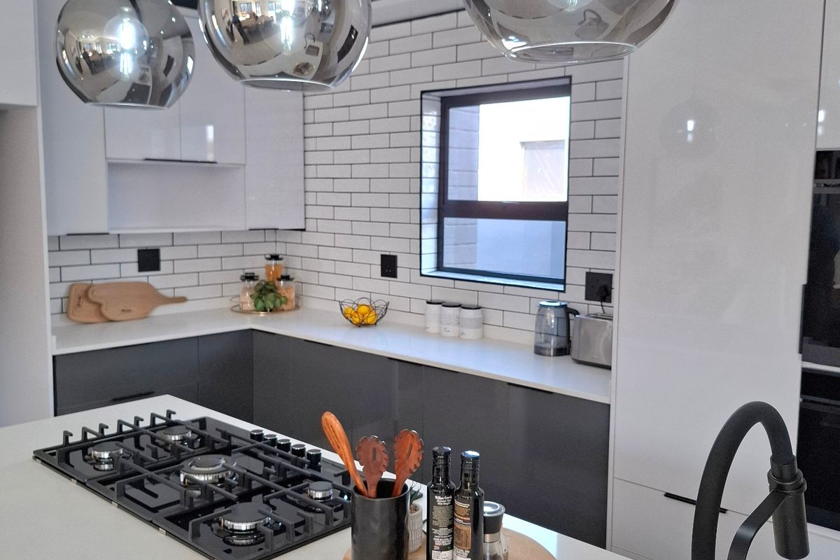 Modern kitchen featuring a central island with a gas hob, sleek white and grey cabinetry, subway tile backsplash, and contemporary pendant lighting.