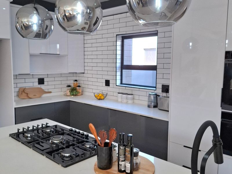 Modern kitchen featuring a central island with a gas hob, sleek white and grey cabinetry, subway tile backsplash, and contemporary pendant lighting.