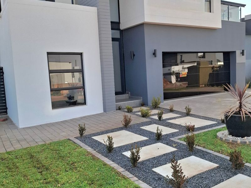 Modern double-story residential facade featuring a sleek grey and white exterior, integrated double garage, and a well-maintained landscaped front garden with stone pathways.