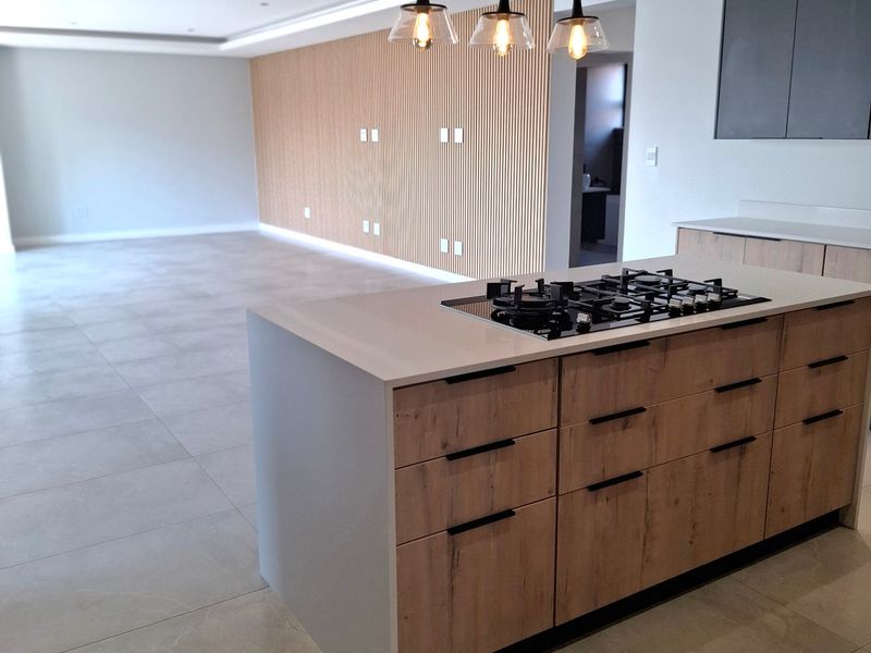 Modern open-plan living area featuring a central kitchen island with gas hob, timber slat feature wall, and large format porcelain floor tiles.
