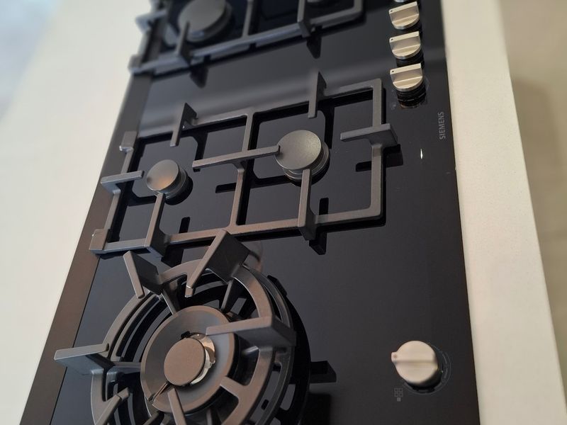 A modern black glass gas cooktop integrated into a clean white stone kitchen countertop.