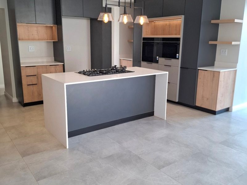 Modern kitchen featuring a central island with a gas hob, sleek dark cabinetry, light wood accents, quartz countertops, and large format floor tiles.