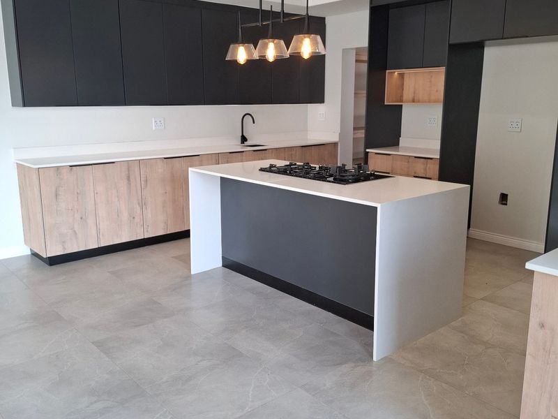 Modern kitchen featuring a central island with a gas hob, sleek two-tone cabinetry, stone countertops, and large format floor tiles.