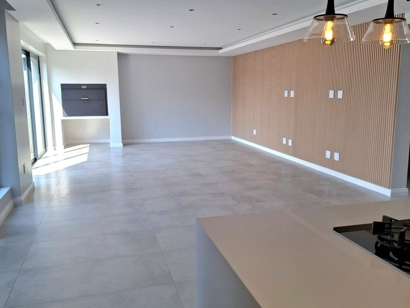 Spacious open-plan living area featuring modern tiled floors, a striking timber slat feature wall, recessed lighting, and a built-in indoor braai.