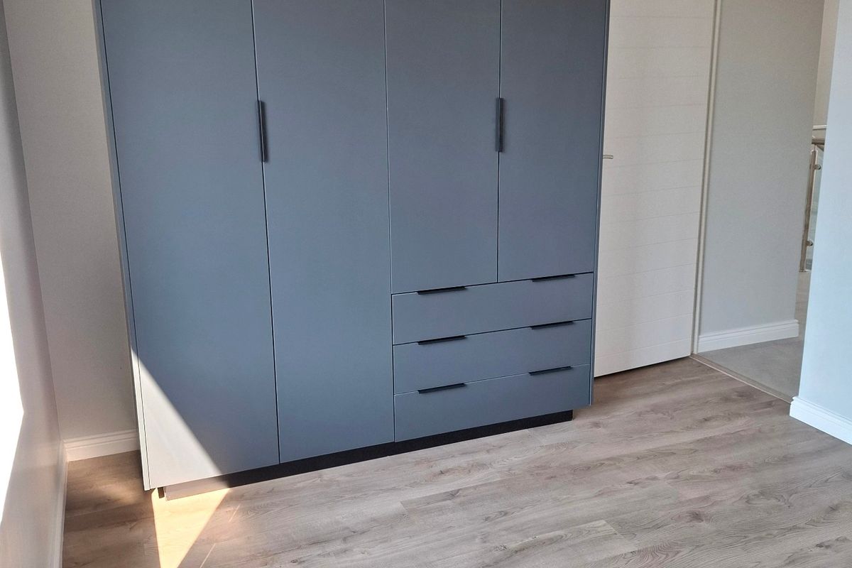 A bright, modern bedroom featuring high-quality laminate flooring and a large, contemporary built-in wardrobe with matte grey finish.