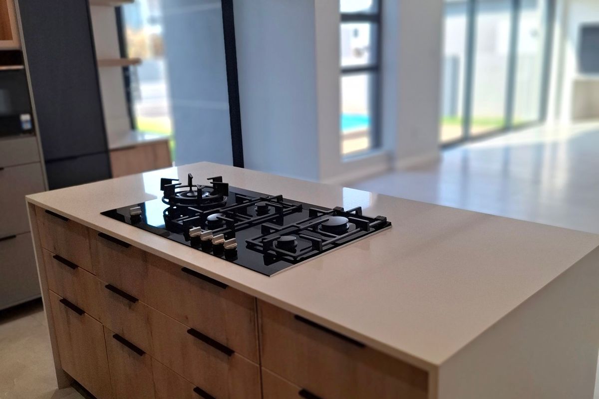 Modern kitchen featuring a central island with a built-in gas hob, stone countertops, and contemporary cabinetry, opening onto a bright, spacious living area.