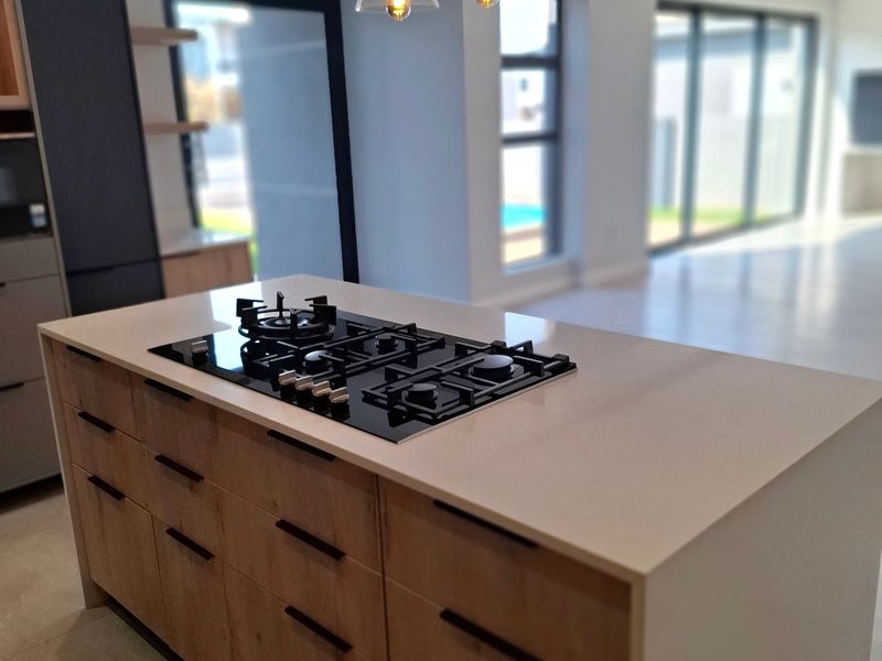 Modern kitchen featuring a central island with a built-in gas hob, stone countertops, and contemporary cabinetry, opening onto a bright, spacious living area.