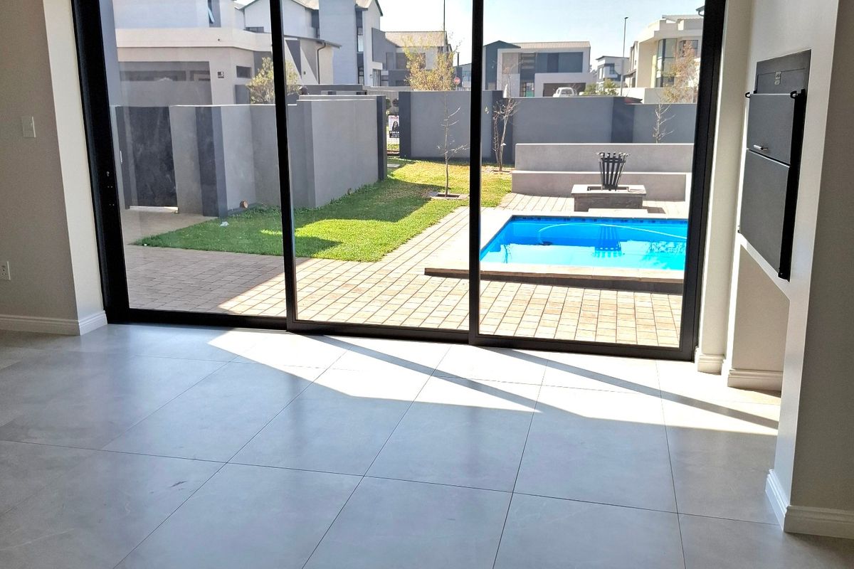 Bright, modern living area featuring large sliding glass doors that open onto a private patio, swimming pool, and landscaped garden.
