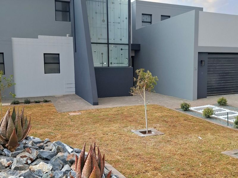 Modern double-storey residential facade featuring a striking glass feature window, integrated garage, and landscaped front garden.