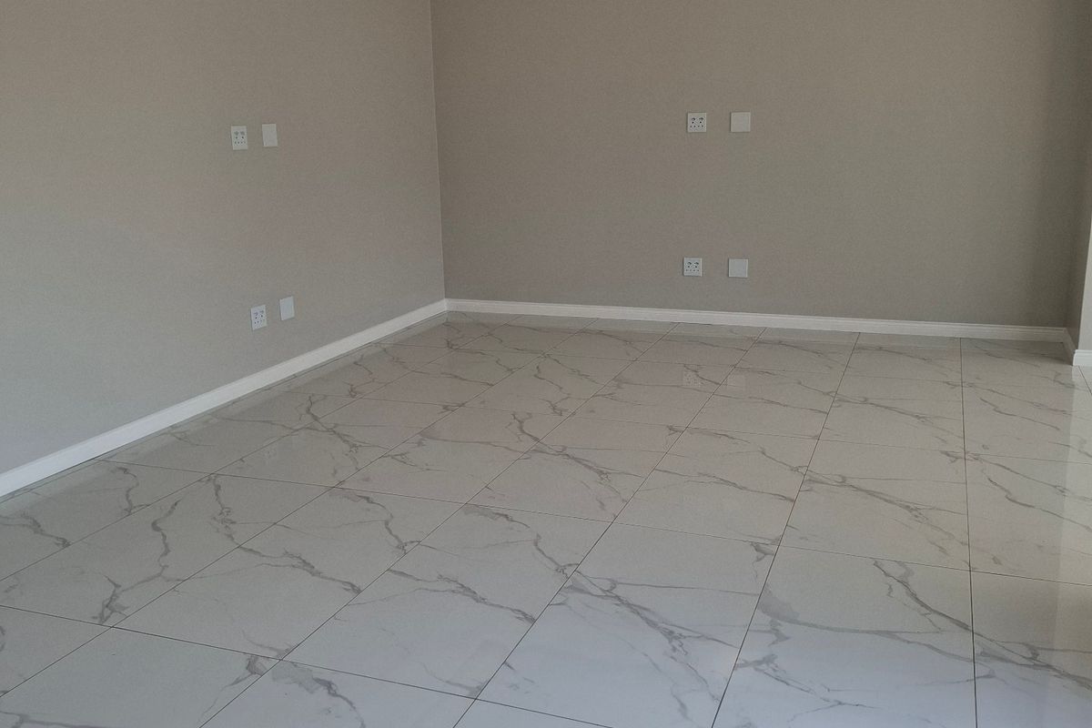 A bright, empty living room featuring modern marble-look floor tiles, clean neutral walls, and a recessed ceiling with integrated lighting.