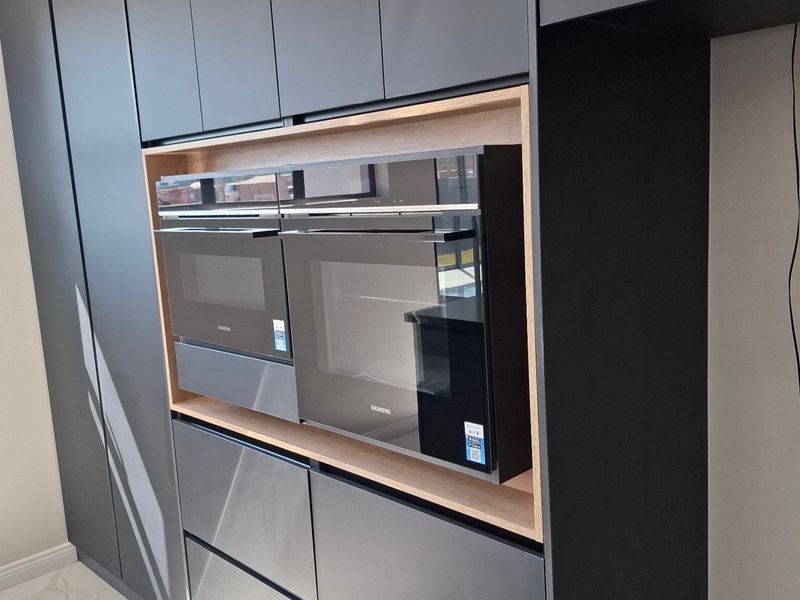Modern kitchen featuring sleek dark grey cabinetry with integrated Siemens oven and microwave, complemented by light marble-look floor tiles.