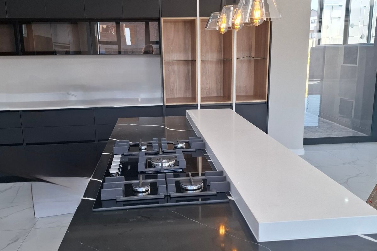 Modern kitchen featuring a sleek black stone island with integrated gas hob, dark cabinetry, and contemporary pendant lighting.