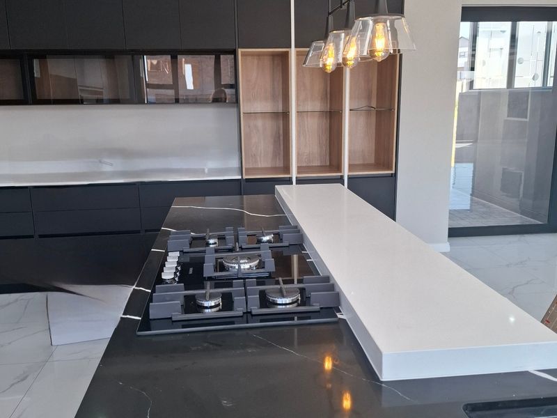 Modern kitchen featuring a sleek black stone island with integrated gas hob, dark cabinetry, and contemporary pendant lighting.