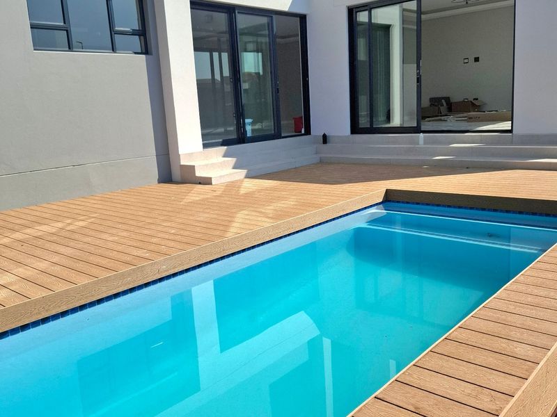 Modern outdoor pool area featuring composite decking, clear blue water, and seamless access to the interior living space through large sliding glass doors.
