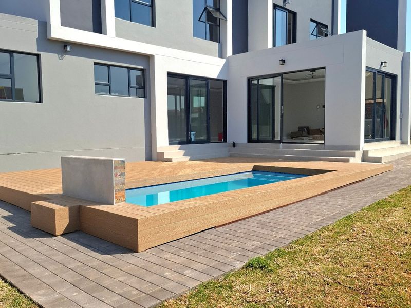Modern rear exterior featuring a contemporary swimming pool with composite decking, paved surrounds, and large sliding glass doors leading into the home.
