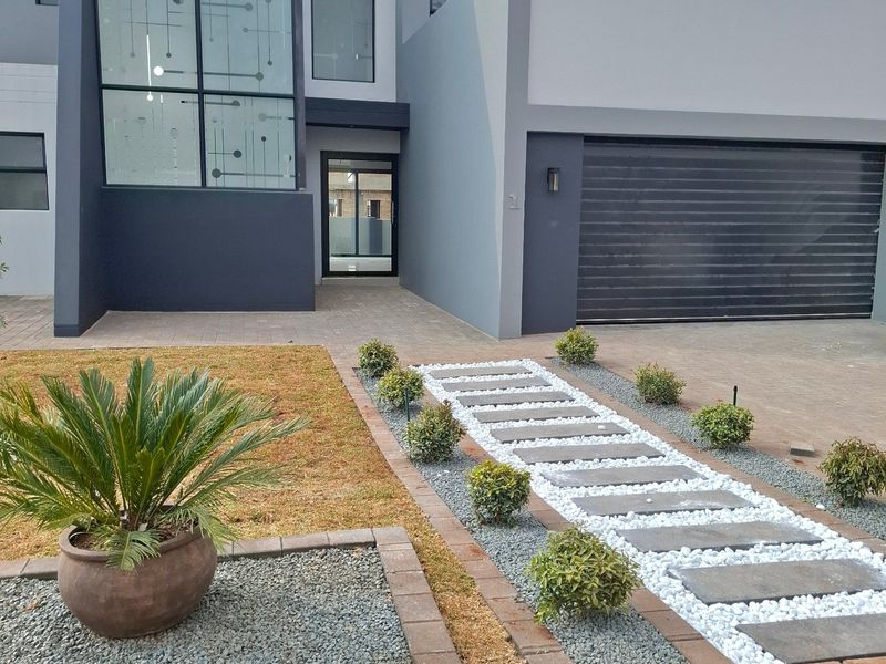 Modern double-story residential facade featuring a sleek garage, decorative glass window detail, and a landscaped stone pathway leading to the entrance.