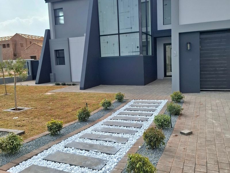 Modern double-storey home featuring a striking architectural facade with a large feature window, paved driveway, and a neatly landscaped stone pathway entrance.