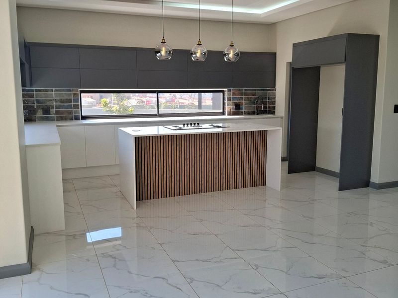 Modern, high-end kitchen featuring a central island with a hob, sleek cabinetry, marble-look tiled flooring, and contemporary recessed ceiling lighting.