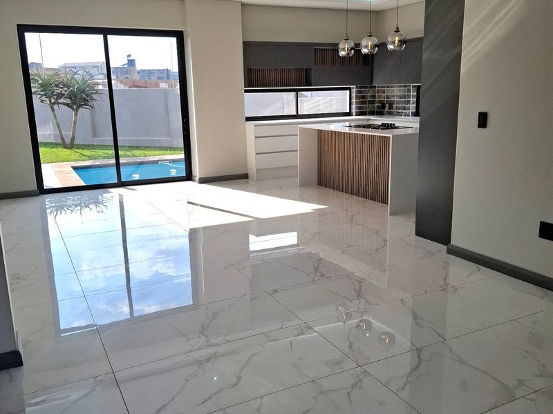 Modern open-plan living and kitchen area featuring high-gloss marble-look floor tiles, recessed ceiling lighting, and direct access to the pool area via sliding doors.