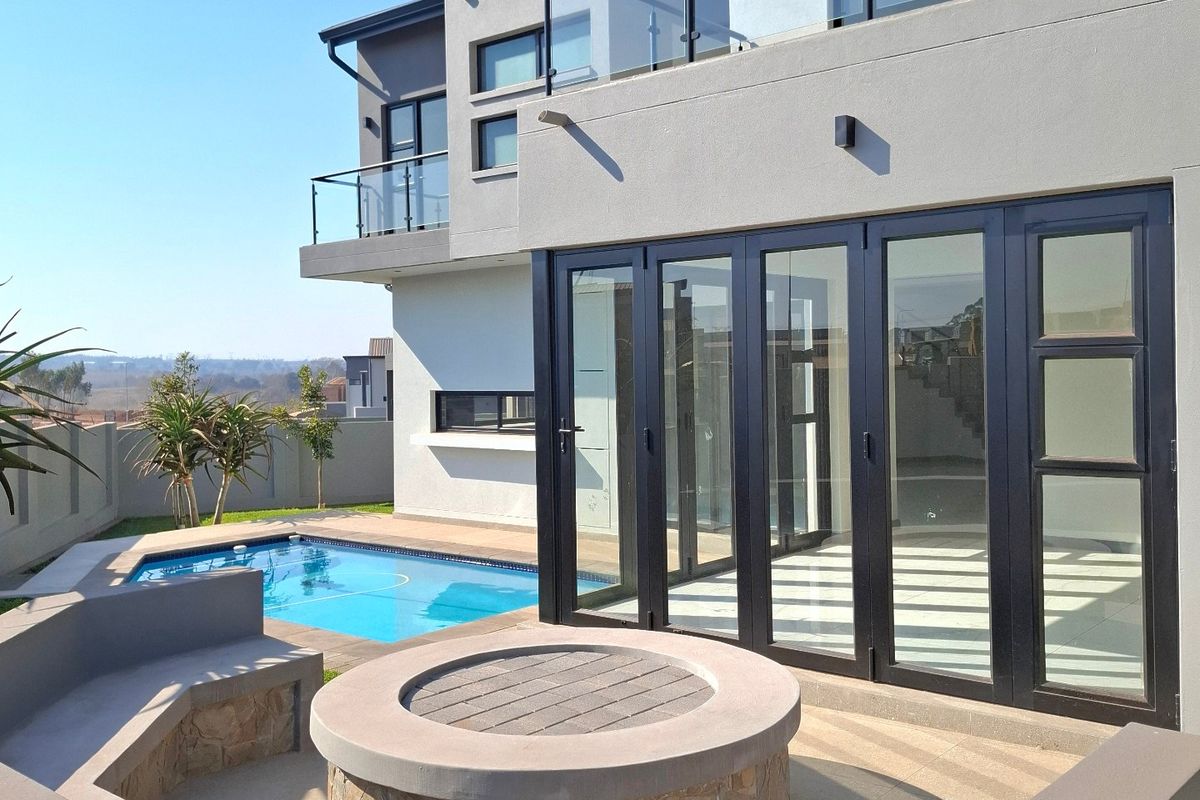 Modern rear exterior featuring a swimming pool, built-in fire pit with seating, and bi-fold doors leading to an upper-level balcony.