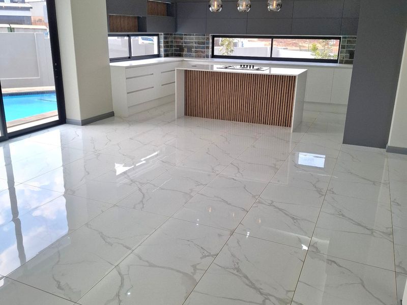 Modern, spacious kitchen featuring a central island with a cooktop, sleek cabinetry, marble-look tiled flooring, and direct access to the pool area.
