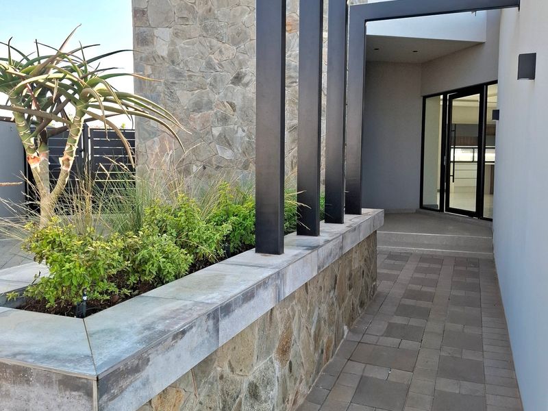 Modern entrance featuring a stone-clad feature wall, a sleek black metal pergola, and a paved walkway leading to a glass front door.