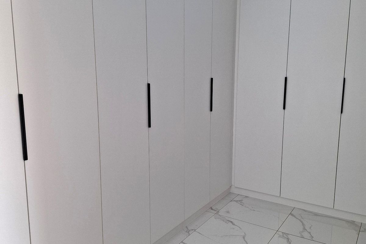 A clean, modern bedroom space featuring floor-to-ceiling white built-in wardrobes and polished marble-effect floor tiles.